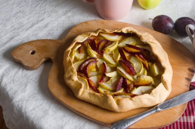 Beyaz keten masa örtüsü üzerinde elma ve erikli ev yapımı galet. Açık turta. Masadaki ev yapımı turta kabuğunun en üst görüntüsü. Kırsal ev yapımı meyveli turta..