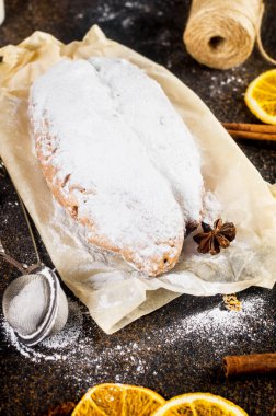 Koyu ahşap masada, ksenli ağaç dalları ve süslemeleri olan kraft kağıdının üzerinde çalınmış. Yılbaşı Alman geleneksel meyveli ekmeği kurutulmuş böğürtlen, fındık ve pudra şekeriyle çalındı.. 