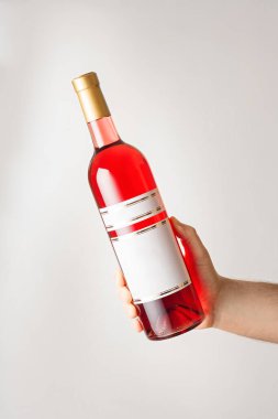 Erkek el, üzerinde marka etiketi olmayan küçük kırmızı yarı tatlı ya da kuru şarap şişesini tutuyor. Sahte şablon. Dikey çekim, beyaz arkaplan