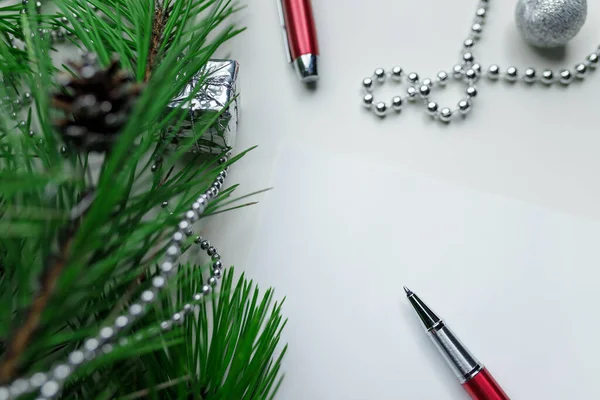 Noel tatili arkaplanı - beyaz masa zemininde beyaz çarşaf ve kırmızı kalemle süslenmiş. Yeni yıl çamı ve gümüş Noel baloları. Üst Manzara. Metin için yer.