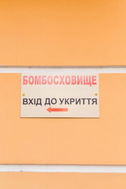 Üzerinde Ukraynaca yazılar olan tabela, Sığınak. Mülteci girişi turuncu duvarda. Ukrayna 2022 'de savaş. Rus istilası. Dikey çekim