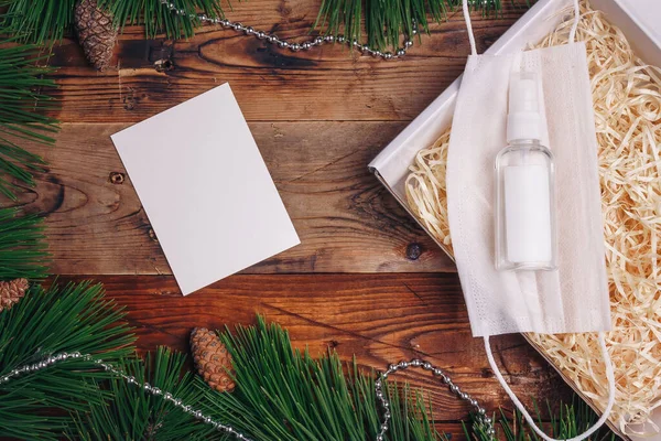 Güvenli Noel, salgın yeni yıl 2021 mevcut kutu konsepti. Covid-19. Çam dalları, koniler, boncuklar, koruyucu gazlı bez maskesi, dezenfektan, ahşap arka planda kağıt kaplama.. 