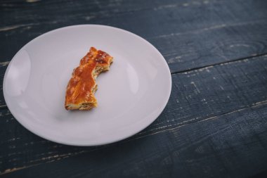 Küçük bir parça ya da bir parça turta, beyaz tabakta siyah tahta masa zemininde kalmış. Lezzetli ve sağlıksız bir ürün. Diyet, beslenme, yeme alışkanlıkları. Az kilolu ya da fazla kilolu. Boşluğu kopyala.