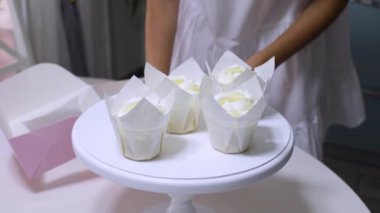 Kız pastacı, beyaz büfeden gelen kekleri masanın üzerindeki pembe kutuya koyuyor. Yaklaş, sadece eller görünür.
