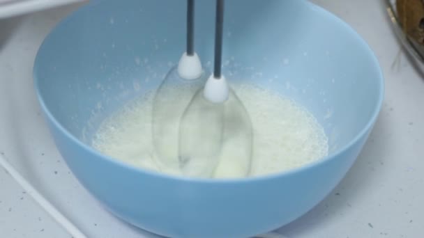 混合器在白色厨房桌子上的蓝色碗中搅拌乳脂 关上镜头 自制食品 烘焙甜糕点 — 图库视频影像