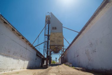 İhracattan önce ambar asansörü deposundan kamyonlara tahıl ve ürün yükleme yeri, mavi gökyüzü arkaplanı.