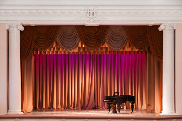 illuminated by lights stage with backstage and decorative columns, there is an old grand piano