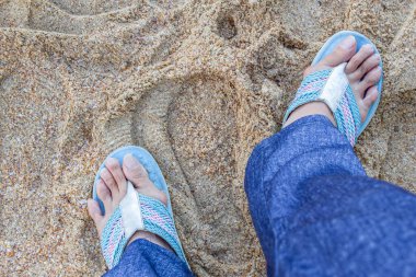 Hallux valgus, pantolonunda nasır olan kadın bacakları kumun üstünde duruyor.