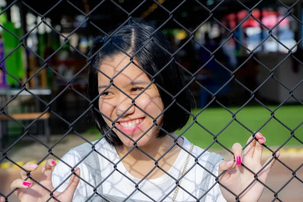 在铁链栅栏后面的亚洲女孩在寻找一个人或观看体育比赛 — 图库照片