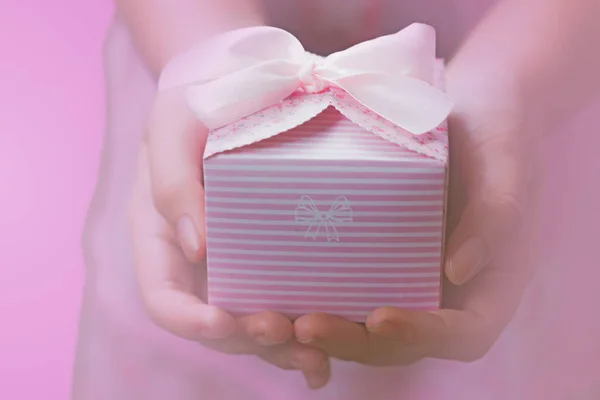 ピンクリボンで包まれた小さなピンクのギフトを保持している女性の手のクローズアップ — ストック写真