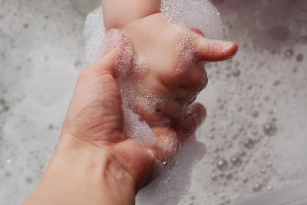 Mãe segura a mão de uma criança em uma banheira com espuma — Fotografia de Stock