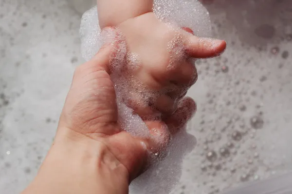 Madre tiene la mano di un bambino in una vasca da bagno con schiuma Immagine Stock