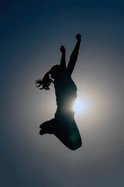 Silhouette of a beautiful woman jumping on the sunset sky.