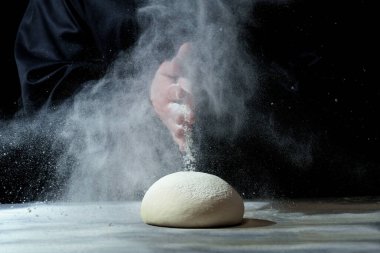 Siyah arka planda el çırpma hamuru. Eller hamurun üzerine un serpiyor. hamur yoğurma.
