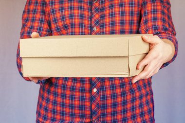 Cropped portrait of woman in plaid shirt holding mail cardboard box with hands in front of her.