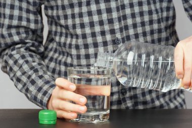 boy pours water from a plastic bottle into a glass.