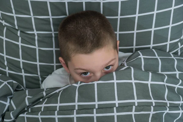 Ein kleiner Junge im Bett bedeckte sein Gesicht mit einer Decke. — Stockfoto