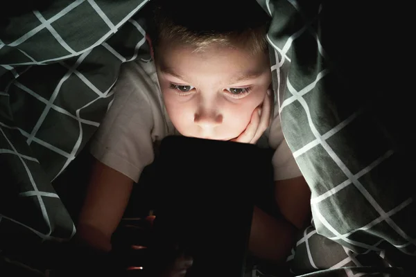 Geceleri battaniyenin altında saklanan bir çocuk telefonuyla oynuyor. Aletlere çocuk bağımlılığı