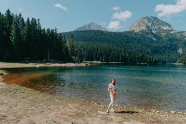 Kız, Karadağ Durmitor Ulusal Parkı 'ndaki Kara Göl, orman ve dağlara bakıyor. Bir turist sihirli bir göl manzarası, kozalaklı bir orman ve sihirli bir manzaranın tadını çıkarır.