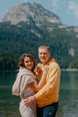 Güzel bir dağ ve gölün kıyısında kucaklaşan çift. Nazikçe sarılıp birbirine aşık çiftin güzel bir doğa geçmişine sahip öpücüğü. Kayalık dağların önünde göl.