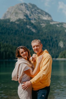 Güzel bir dağ ve gölün kıyısında kucaklaşan çift. Nazikçe sarılıp birbirine aşık çiftin güzel bir doğa geçmişine sahip öpücüğü. Kayalık dağların önünde göl.