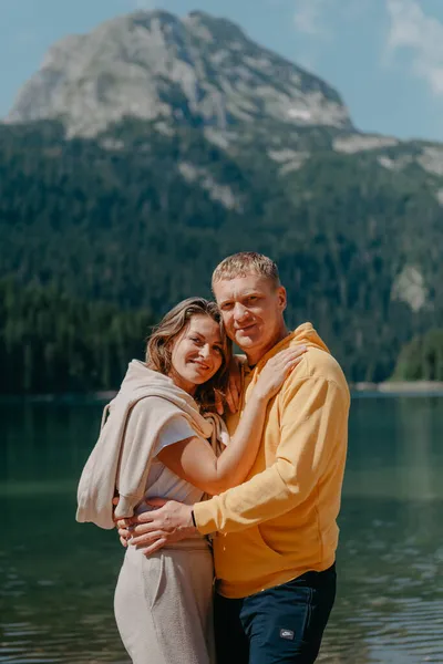 Casal abraçando na margem de uma bela bela montanha e lago. abraços suaves e beijo do casal apaixonado em um belo fundo de natureza. lago em frente a montanhas rochosas. — Fotografia de Stock