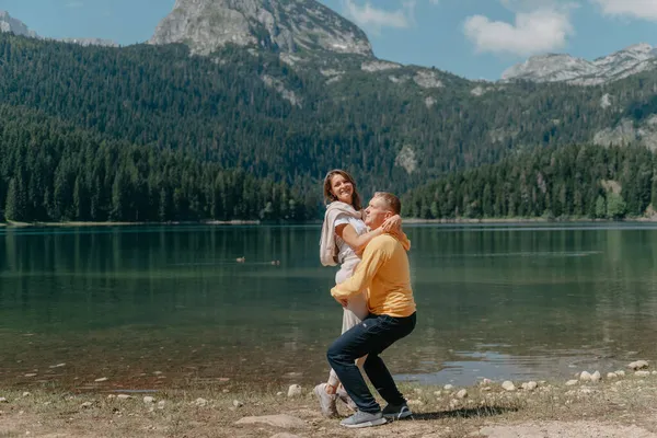 Casal abraçando na margem de uma bela bela montanha e lago. abraços suaves e beijo do casal apaixonado em um belo fundo de natureza. lago em frente a montanhas rochosas. — Fotografia de Stock