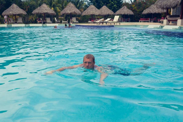 Feliz hombre atractivo nada en el agua azul de una piscina. Resort al aire libre, hotel de lujo. spa de verano cerca del mar. Paraíso Tropical. República Dominicana, Seychelles, Caribe, Bahamas. — Foto de Stock