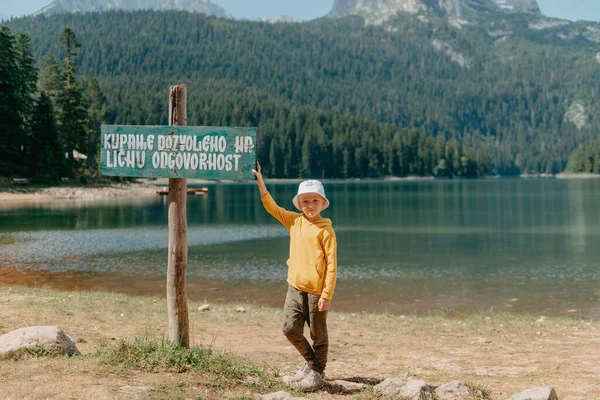 少年は、山の湖、黒湖、デュルモーター国立公園、モンテネグロ、ヨーロッパの海岸に立っています。セルビア語での説明:入浴は個人の責任で許可されています — ストック写真