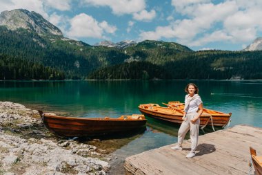 Kız, Karadağ Durmitor Ulusal Parkı 'ndaki balıkçı tekneleri, ormanlar ve dağlarla Kara Göl' e bakıyor. Bir turist sihirli bir göl manzarası, kozalaklı bir orman ve büyülü bir manzaranın tadını çıkarır.