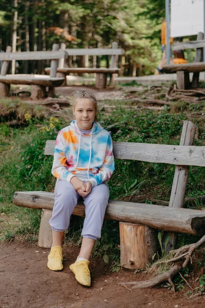Χαριτωμένο έφηβο κορίτσι κάθεται σε ένα ξύλινο παγκάκι στο πάρκο — Φωτογραφία Αρχείου