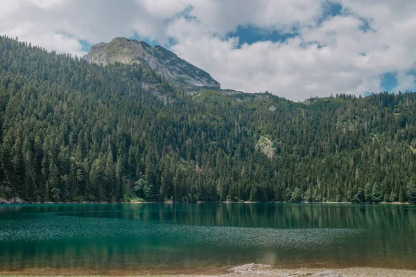 Bela vista do lago de esmeralda. Água azul-turquesa clara reflete a montanha coberta de neve, pinheiros altos que alinham a costa e nuvens brancas em um céu azul. — Fotografia de Stock