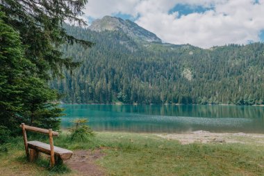 Rahat ol. Göl kenarında dinlen. Göle ve dağlara bakan ahşap bir bank. Güzel mistik göl. Kara Göl, Durmitor Ulusal Parkı. Karadağ
