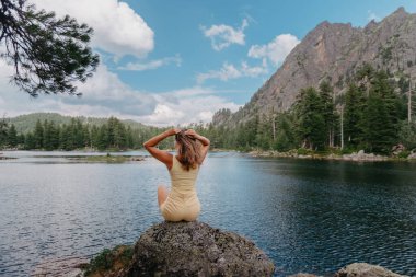 Turist kız gölün, kozalaklı ormanın ve dağlardaki turkuaz gölün kıyısındaki büyük taşın üzerindeki sihirli manzaranın tadını çıkarıyor. Doğal Park 'ta yürüyüş. Tatlı kız.