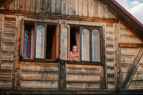 Porträt eines schönen Mädchens am Fensterrahmen eines hölzernen Waldhauses. Junges Teenager-Mädchen im Fenster eines Holzhauses in den Bergen. Ruhige Erholung, allein mit der Natur. Im Einklang mit sich selbst — Stockfoto