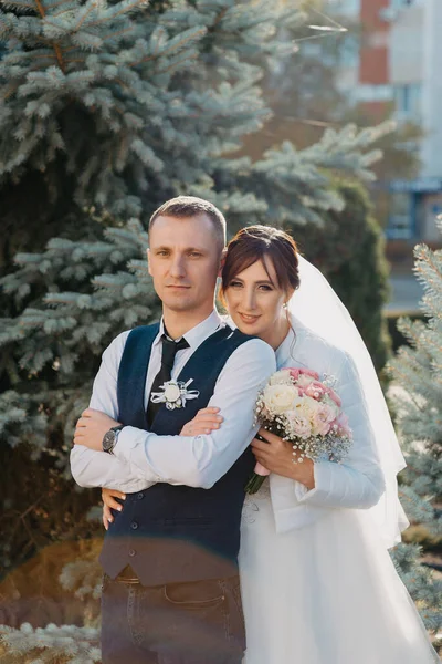Elegáns menyasszony és a vőlegény pózol együtt a szabadban egy esküvő napján. Vőlegény és menyasszony egy parkban. esküvői ruha. Menyasszonyi esküvői csokor virág — Stock Fotó