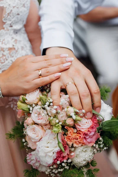 Las lunas de miel tienen las manos en una bolsa de flores para bodas. Manos y anillos en el ramo de bodas —  Fotos de Stock