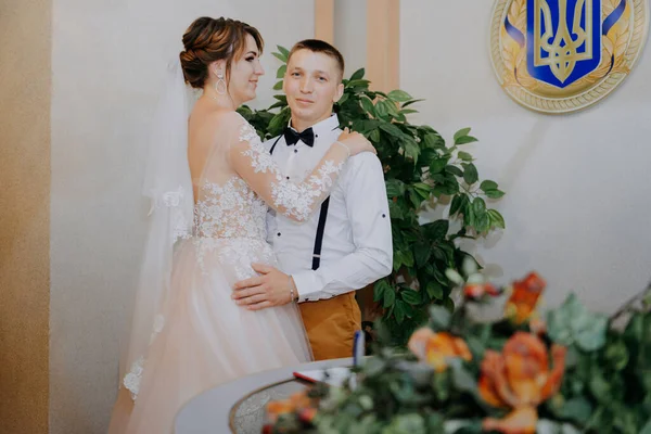 Wedding: young couple in love bride and groom hugging each other holding a bouquet of flowers. Two lovers hearts on the wedding ceremony. Stylish happy smiling newlyweds. Bride and groom look at each — Stock Photo, Image