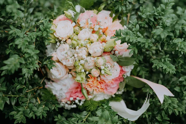 Look from above at white nd pink wedding bouquet of flowers lying on the bush. A beautiful bridal bouquet of white roses lies on a green bush. Soft focus. — Stock Photo, Image