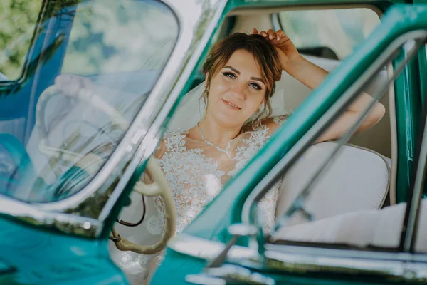 結婚式の花嫁の残りの部分と結婚式後の緑のヴィンテージレトロな車でお楽しみください。新婚旅行のコンセプト。車の女性は古いレトロなヴィンテージ車で幸せ。美しい晴れた夏の日に道路の旅に運転若い女性. — ストック写真