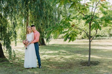 Gelin ve damat gün açık havada yürüyüş düğününde doğa bahar. Gelin Çift, mutlu yeni evli kadın ve yeşil park kucaklayan adam. Sevgi dolu evlilik çift açık. Gelin ve damat, düğün çekim