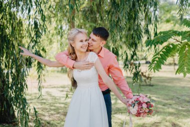 Gelin ve damat gün açık havada yürüyüş düğününde doğa bahar. Gelin Çift, mutlu yeni evli kadın ve yeşil park kucaklayan adam. Sevgi dolu evlilik çift açık. Gelin ve damat, düğün çekim