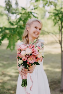 Açık havada çiçekli gelin. Orman parkında bir buket çiçekle uzun beyaz gelinlik içinde güzel bir gelinin portresi. Moda gelinliği içinde, doğal bir geçmişi olan güzel bir gelin.