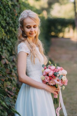 Açık havada çiçekli gelin. Orman parkında bir buket çiçekle uzun beyaz gelinlik içinde güzel bir gelinin portresi. Moda gelinliği içinde, doğal bir geçmişi olan güzel bir gelin.
