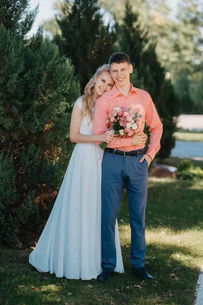 Noiva e noivo no dia do casamento andando ao ar livre na natureza de primavera. Casal nupcial, mulher recém-casada feliz e homem abraçando no parque verde. Casal de amor ao ar livre. Tiro de casamento de noiva e noivo em — Fotografia de Stock