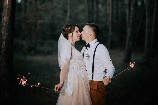 Νιόπαντροι με βεγγαλικά σε νυχτερινό πάρκο. Οι νιόπαντροι φιλιούνται και κρατούν τη σπίθα. Ένα τέλειο τέλος για την ημέρα του γάμου. Πυροβολισμοί στο σκοτάδι. η νύφη σε ένα λευκό κομψό φόρεμα και ο γαμπρός σε ένα λευκό — Φωτογραφία Αρχείου