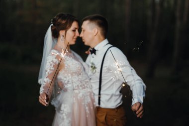 Gece parkında maytaplı yeni evliler. Yeni evliler maytapları öpüp tutarlar. Düğün günü için mükemmel bir son. Karanlıkta ateş etmek. Beyaz elbiseli gelin ve beyaz elbiseli damat.