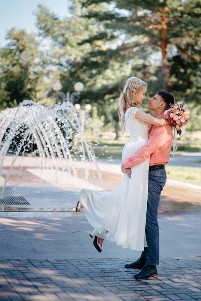 噴水の近くの結婚式の歩く上で幸せな花嫁と新郎。花嫁と新郎は結婚式の日にロマンチックな瞬間を持っています. — ストック写真