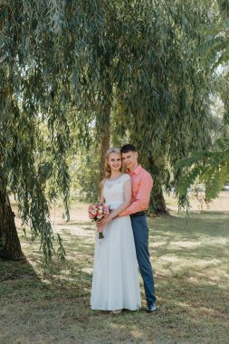 Gelin ve damat gün açık havada yürüyüş düğününde doğa bahar. Gelin Çift, mutlu yeni evli kadın ve yeşil park kucaklayan adam. Sevgi dolu evlilik çift açık. Gelin ve damat, düğün çekim