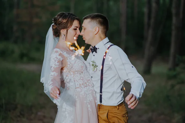 Nygifta med tomtebloss i en nattpark. De nygifta kysser och håller i tomtebloss. Ett perfekt slut på bröllopsdagen. skjuta i mörkret. bruden i vit elegant klänning och brudgummen i vit — Stockfoto